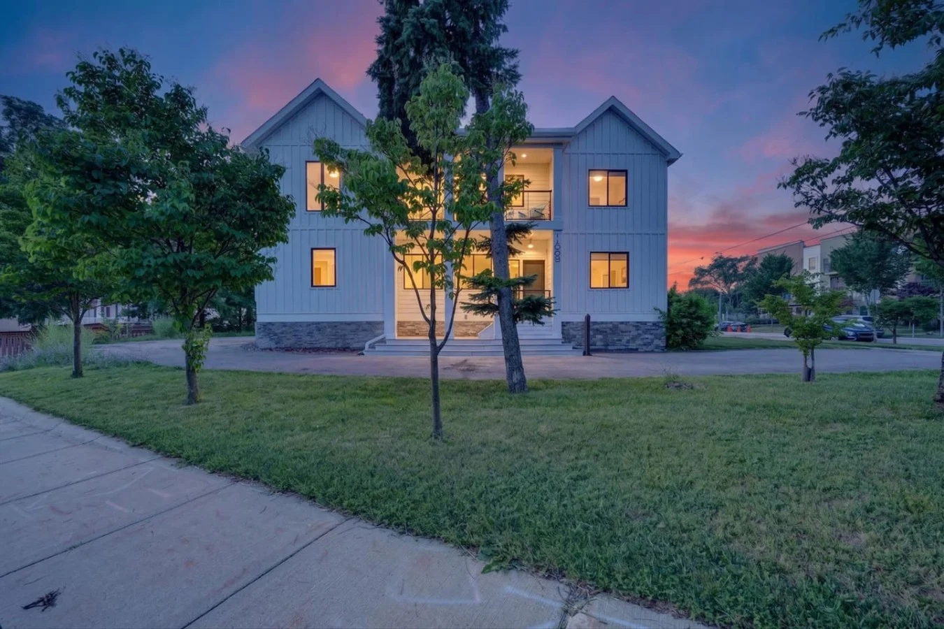 Ann Arbor home with a white facade, lit windows and lawn at dusk